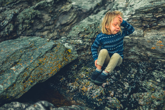 Little preschooler sitting on rocks in nature