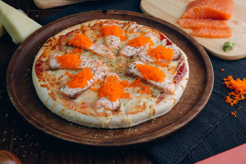 Salmon pizza topped with ebiko in a brown wooden plate