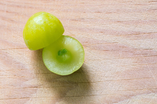 Una uva verde y jugosa partida en dos, con la semilla de la uva a la vista, sobre una tabla de madera