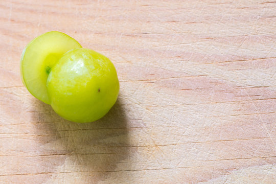 Una uva verde y jugosa partida en dos, con la semilla de la uva a la vista, sobre una tabla de madera
