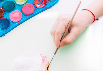 Child hands painting white clay figure with colored watercolors. Painting, education and relaxation concept.
