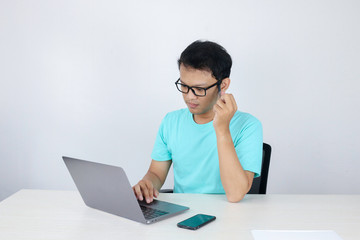 Young Asian Man is serious and focus when working on a laptop on the table. Indonesian man wearing blue shirt.