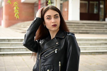 Portrait of a cute young caucasian brunette girl in a black jacket in various poses. Model posing in the city in the spring outdoors.