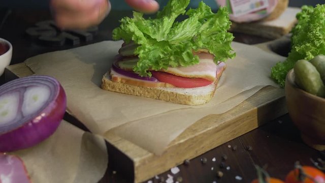 making thesandwich  with sliced bacon pickle and vegetables on the wooden board