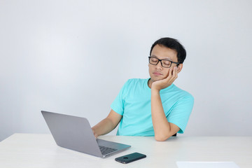 Young Asian Man is Lazy and tired with sleep when working in the front of Laptop. Indonesian man wearing blue shirt.