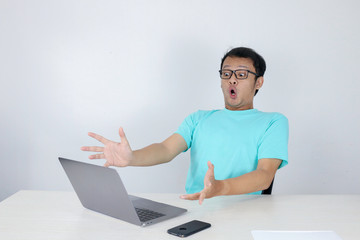 Wow face of Young Asian man shocked what he see in the laptop when working isolated grey background wearing blue shirt.