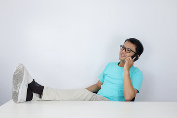 Fototapeta premium Young Asian man is feeling happy and smile face when talk on the phone with leg on the table.