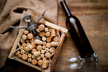Wine corks of different sizes, a corkscrew, a bottle of wine and a glass shot on an old wooden surface. Background for liquor.