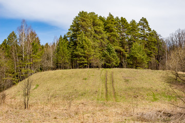 Fototapeta premium Landscape with a hill in a forest area. Ichinskoe (Ichskoe, Altukhovskoe) ancient settlement on the river Icha. Zhukovsky District, Zhukovskiy Region, Russia - April 2020