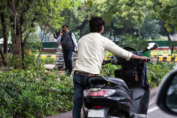 A Indian man pushing his bike as he walks along due to scooter breakdown on the streets. Rear view of stranded person on road after motor vehicle engine failure as it ran out of petrol gas in Delhi.