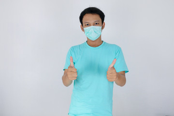 Young Asian Man wear medical mask is give ok hand sign with confident gestures. Indonesian man wearing blue shirt.