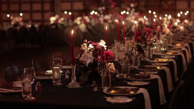 Panning showing the decoration of the tables for a wedding reception dinner, with dark red lit candles
