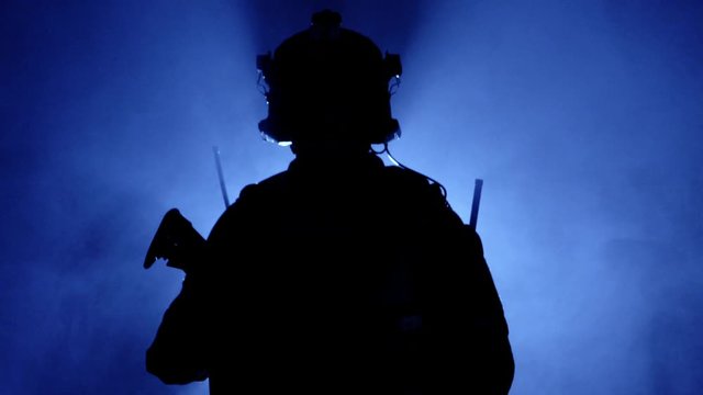 Military soldier in military equipment with a firearm in smoke on a blue background. Backlight, military operations. American army, slow motion