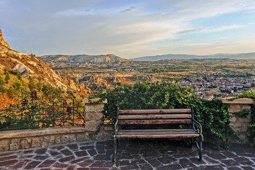 A great place to relax in magical Cappadocia. A bench braided by green vines stands on a mountain platform. It offers amazing views of the mountains, the valley and a small settlement. Sunny day.