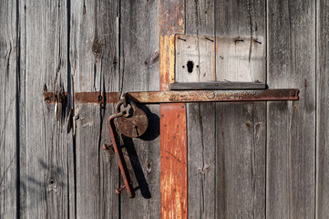 Old wooden barn door with rusty metal padlock.