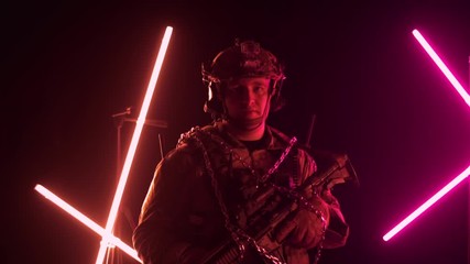 a serious caucasian soldier in a military outfit with a weapon stands and looks at the camera. Metal chains and soldiers, captive and hostage concept, slow motion