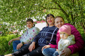 Fototapeta premium Three different funny women and one small seriously girl in the park full of apple blossom trees in a spring day. Aunts and niece in nature landscape