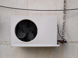 A black fan on an old air compressor cabinet with a broken grille on a white plaster wall...