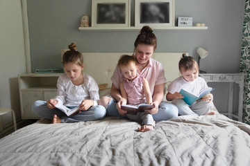 mother reads a book with three children in bed