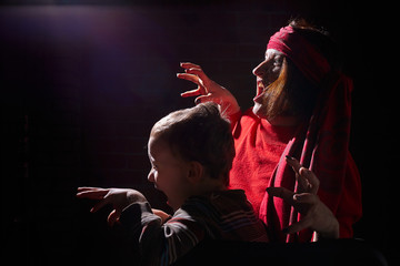 Woman in red sweater and the turban of wizard or sorcerer with boy on black background. Actress...