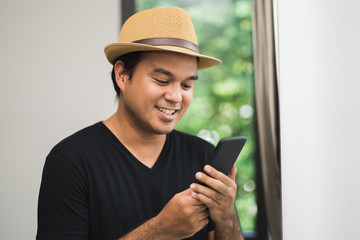 A young Asian man uses a smartphone. He is around 30 Wearing a black shirt, wearing a hat Stay in his house