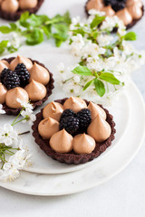 Chocolate tart with caramel filling and fresh blackberries. Cherry flowers on background. Copy space