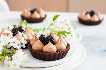 Chocolate tart with caramel filling and fresh blackberries. Cherry flowers on background. Copy space