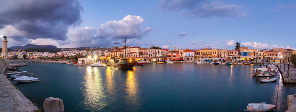Venetian Harbour panorama with boats in front of restaurants at sunrise under colored clouds. Rethymno, Crete, Greece