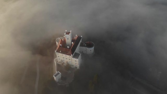 Aerial view of an old middle age kingdom castle on the top of hill covered in mist and fog during an epic sunrise. Cinematic drone footage