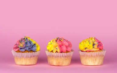 Homemade cupcakes with multi-colored cream on a pink background copy space. Yellow and pink cream. Cupcakes with confetti. Birthday cakes.