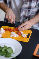 Fototapeta premium Male hands cutting cherry tomatoes and mushrooms.