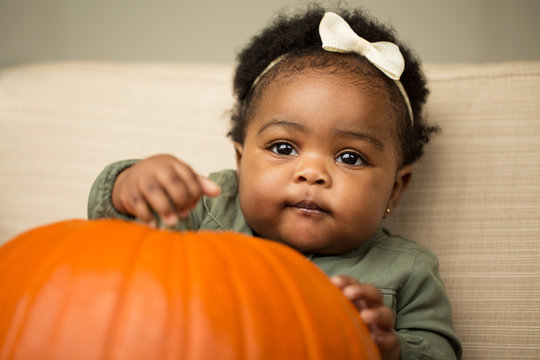 Cute African American little girl holding a pumpkin.