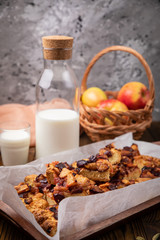 Home made apple pie on a tray, on a brown background. Glass and bottle of milk, basket with apples