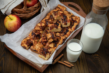 Home made apple pie on a tray, on a brown background. Glass and bottle of milk, basket with apples