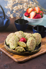 Matcha madeleine cookies with green tea and white chocolate frosting on dark background with teapot and cups. Almond vegan pastry treat made with flax eggs