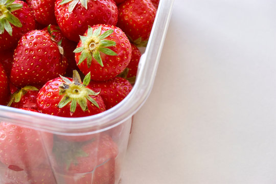 Fresh ripe strawberries in a clear plastic container on white background. Image with copy space.