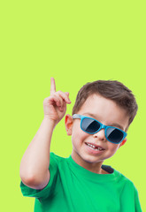 Cheerful little boy in sunglasses showing thumbs up gesture, on green background