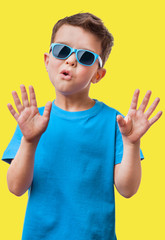 Little boy in sunglasses raised his hands up, on yellow background
