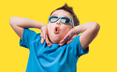 Cheerful little boy in sunglasses express surprised face, isolated on yellow background