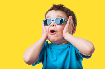 Cheerful little boy in sunglasses express surprised face, isolated on yellow background