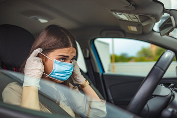 Woman during pandemic isolation at city, she is in car. Young woman driving car with protective mask on her face. Healthcare, virus protection, allergy protection concept.