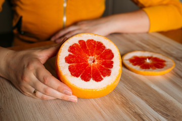  Cut grapefruit in hands of a person indoors at home. The colors of the clothes and the colors of the fruit match. Close up.