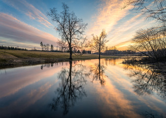 Beautiful sunset glow with calm landscape with tree reflections and sunlight at spring evening in river Finland