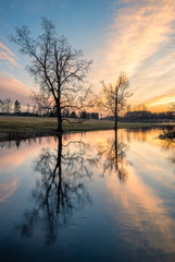 Beautiful sunset glow with calm landscape with tree reflections and sunlight at spring evening in river Finland