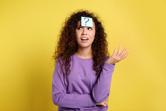 Emotional African-American woman with question mark sticker on forehead against yellow background