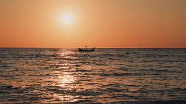 Beautiful sunset at the sea. Small fisherman boat rocking on waves on a horizon. Orange tropical sunset in Phuket, Thailand. Golden sunset with sunlight reflecting off waves. Seascape.