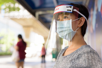 Face of young Asian woman wearing mask and face shield while sitting at the bus stop