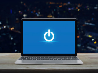 Power button icon on modern laptop computer on wooden table over blur colorful night light office...