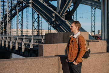 A business man in a beige jacket and with a backpack walks in Sunny weather on the beautiful drawbridge over the Neva river in St. Petersburg, an architectural monument, a metal bridge with towers