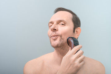 handsome man shaves with an electric razor, funny facial expressions